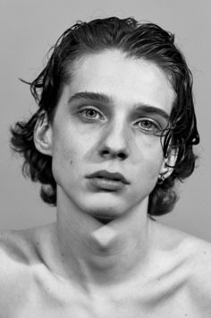 a black and white photo of a young man with curly hair looking at the camera