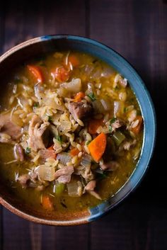 a blue bowl filled with meat and rice soup on top of a wooden table next to a spoon