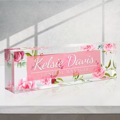 a glass sign with pink flowers on it that says kelsie davis general manager