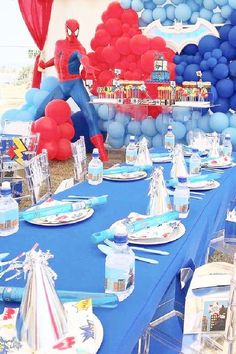 a spiderman birthday party with blue and red table cloths, plates, silverware and balloons