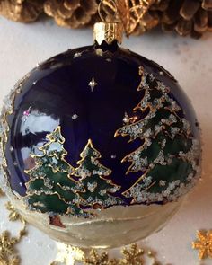 a glass ornament with gold trimmings and christmas trees on it's side