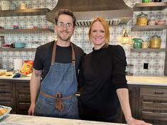 a man and woman standing next to each other in front of a counter with food on it