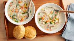 two bowls of chicken pot pie soup on a tray next to rolls and a spoon