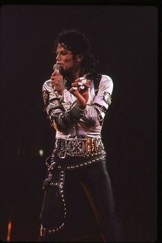 michael jackson performing on stage with his microphone in his right hand and wearing studded pants