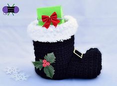 a crocheted christmas stocking with holly and red bow on the top, sitting next to a snowflake