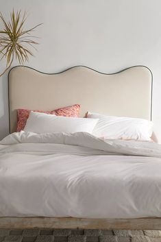 a bed with white linens and pillows in a small room next to a potted plant