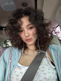 a young woman with curly hair wearing headphones in the back seat of a car