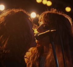 two women standing next to each other with microphones in front of them and lights behind them