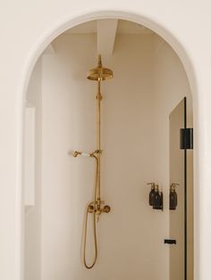 an arched doorway leads into a bathroom with white walls and flooring, along with a gold shower head