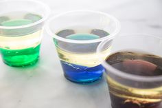 three cups filled with different colored liquids on top of a white countertop next to each other