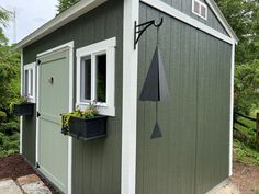 a small green shed with an umbrella on the window sill and flower boxes below