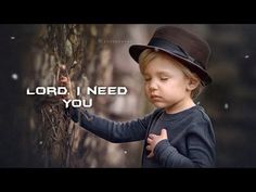 a little boy wearing a hat and holding his hand on the side of a tree