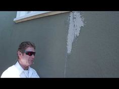 a man wearing sunglasses standing in front of a wall that has some white paint on it