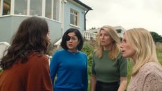 three women standing in front of a house talking to each other