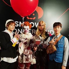 four people dressed in costumes standing next to each other and holding a red heart balloon