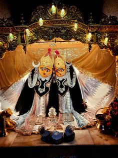 two masks sitting on top of a table in front of a gold cloth covered stage