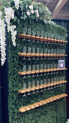 a wall covered in plants and glasses filled with wine is displayed at the reception table