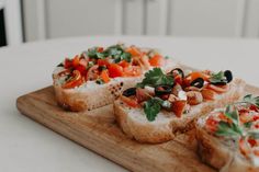 several pieces of bread with various toppings sitting on a wooden cutting board next to a white table