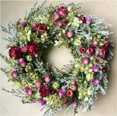 a wreath with purple flowers and greenery on the front is displayed against a beige background