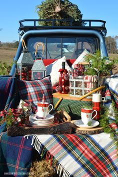 a blue truck with plaid blankets and christmas decorations on it's bed is parked in the grass