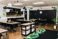 an empty restaurant with tables and chairs, plants on the counter top and black cabinets