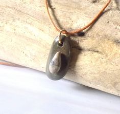 This pendant is made with a coastal stone, either ocean or river. The stone is not tumbled or shaped but is in its natural form, except for the drilled hole. Therefore, the stone/rock will have its natural "imperfections" just as nature made it. This adds character and uniqueness to the piece. They make a perfect gift for rockhounds, yoga\ Zen lovers, surfers or just anyone who loves the beauty of nature. Two stones are used to create this pendant. The small stone is a teardrop shape with interesting soft coloration. The entire piece is coated with a high gloss sealer to give it a nice sheen and protect the design. Pendant has a metal split ring and hangs on an adjustable wax cotton cord with pull apart clasp.  To adjust the length of the cord: 1. pull  open the clasp; 2. push knot through Rock Necklace, Zen Style, Natural Form, Natural Rock, Pull Apart, Rock Hounding, Beach Lovers, Split Ring, Stone Rocks