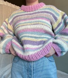 a woman standing in front of a bed with her hands on her hips wearing a colorful sweater