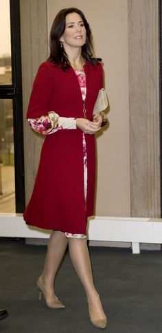 a woman in a red coat and dress walking down the street with her hand on her hip