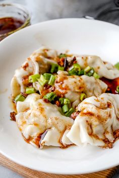 a white plate topped with dumplings covered in sauce and green onions on top of a wooden cutting board