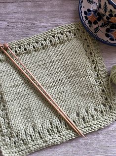 the knitting needles are next to an empty knitted dishcloth