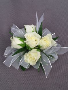 a bouquet of white roses with green leaves on a gray cloth background, ready to be used as a boutonniere