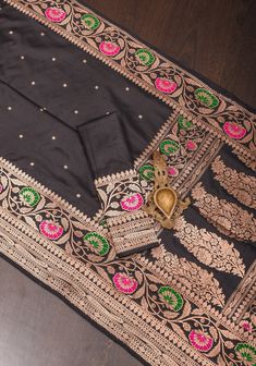 This breathtaking black saree showcases a contemporary interpretation of Banaras' classic weaving techniques. Adorned with intricate chunri zari buttas throughout the body, it is accompanied by a vibrant meenakari Zari floral border and pallu, infusing the luxurious silk fabric with a pop of color. If you admire a unique blend of design, texture, and shades, this saree will captivate your senses. SILK MARK CERTIFIED This saree is ready to wear with fall and pico done. Handmade silk tassels adorn the pallu and add more grace to it. An unstitched blouse fabric is included. *Note: There may be minor variations in the shade, the texture of the product. Hues/textures show differently due to variations in screen settings and other factors, *Note: This saree is woven of pure natural silk, there m Black Art Silk Pre-draped Saree With Zari Weaving, Black Pre-draped Saree With Zari Weaving For Puja, Festive Black Pre-draped Saree With Self Design, Designer Black Pre-draped Saree For Eid, Designer Wear Black Pre-draped Saree For Eid, Traditional Black Pre-draped Saree, Black Pre-draped Saree With Zari Weaving In Art Silk, Festive Black Chanderi Lehenga, Black Chanderi Pre-draped Saree With Self Design