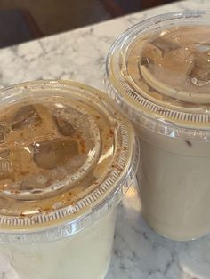 two plastic cups filled with ice cream on top of a marble counter next to each other