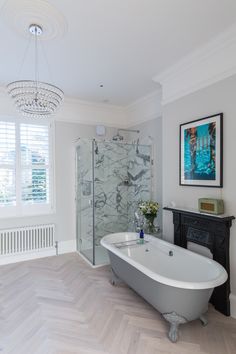 a white bath tub sitting next to a wooden floor in a bathroom under a chandelier