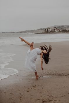 a woman is dancing on the beach with her hair blowing in the wind and she's wearing a white dress