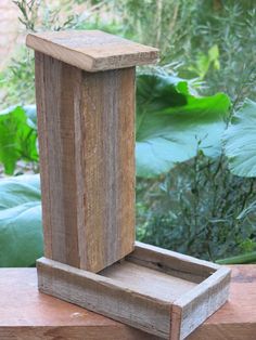 a wooden bird feeder sitting on top of a wooden table next to green plants and bushes