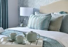 a tray with two tea cups on top of it next to a bed covered in blue and white sheets