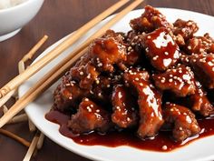 a white plate topped with meat covered in sauce and chopsticks