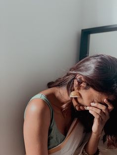 a woman sitting in front of a mirror with her hand on her face while eating food