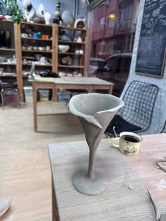 a white vase sitting on top of a wooden table next to a cup and saucer