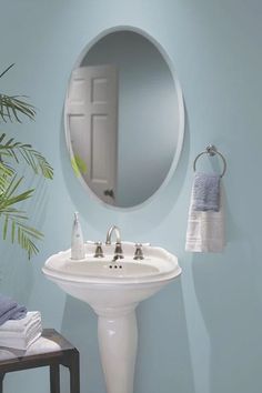 a white sink sitting under a round mirror next to a wooden stool and potted plant