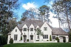 a large white house sitting in the middle of a lush green field next to trees