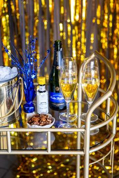 two glasses of wine are sitting on a bar cart with gold tinsel behind it