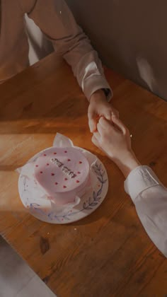 two people holding hands over a cake on a table