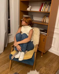 a woman sitting in a chair next to a book shelf with books on top of it