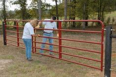 two people standing behind a red fence looking at something on the ground in front of them