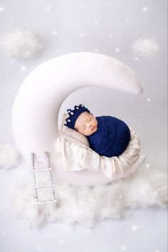 a baby sleeping on top of a crescent in the snow with stars and clouds around it