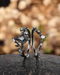 two silver rings with diamonds on them sitting on top of a black rock in front of some rocks