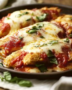 two pieces of chicken parmesan in a skillet with fresh basil on top