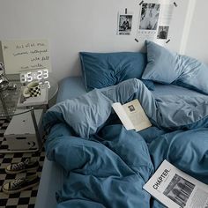 an unmade bed with blue comforter and pillows on it in a room with black and white checkered flooring